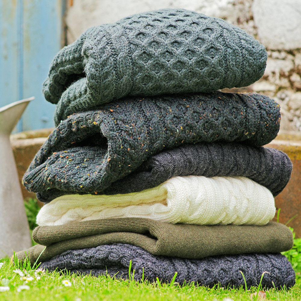 Folded Aran knitwear in various muted colours piled up on grass